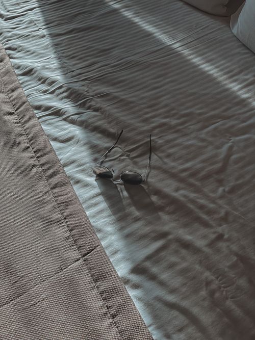 Free Minimalist close-up of sunglasses on a sunlit bedspread, evoking a serene and relaxed atmosphere. Stock Photo