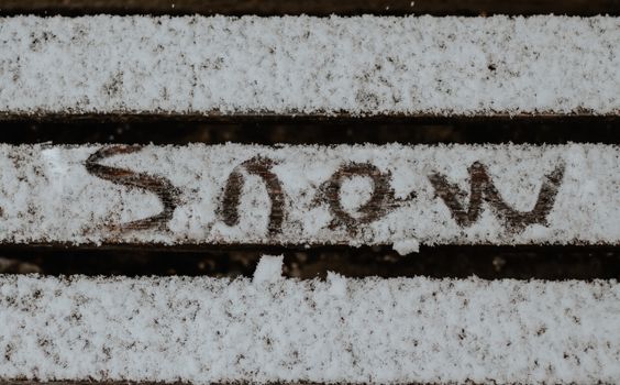 Snow covered wooden slats with 'snow' written in them, conveying winter chill.
