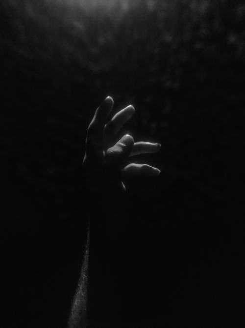 Free A mysterious and dramatic black and white image of a hand reaching out in darkness. Stock Photo