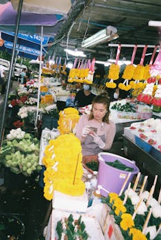A woman arranging flowers at a vibrant market stall in Chiang Mai, Thailand.