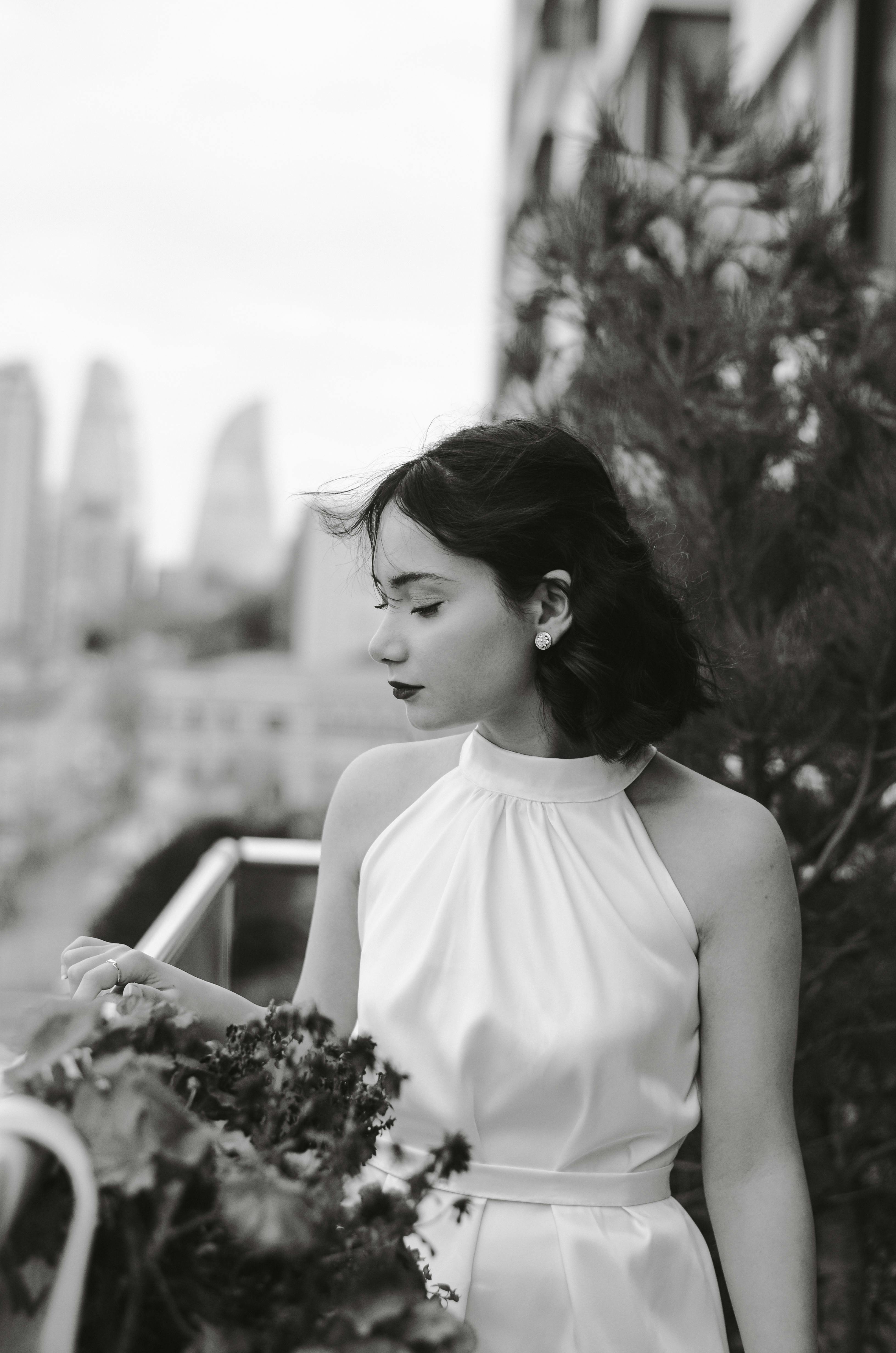 A sophisticated black and white portrait of a woman in a white dress, posing thoughtfully outdoors in Baku, Azerbaijan.