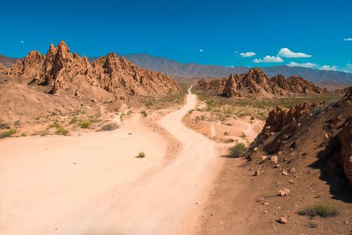 Free A winding dirt road stretches through a dramatic desert landscape with eroded rocky formations and a clear blue sky. Stock Photo