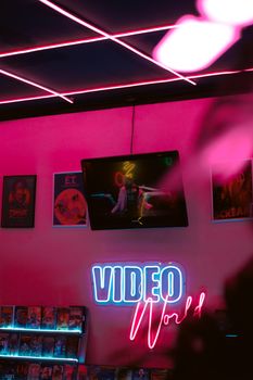 Neon-lit retro video store with pink walls, vintage posters, and a glowing 'Video World' sign.