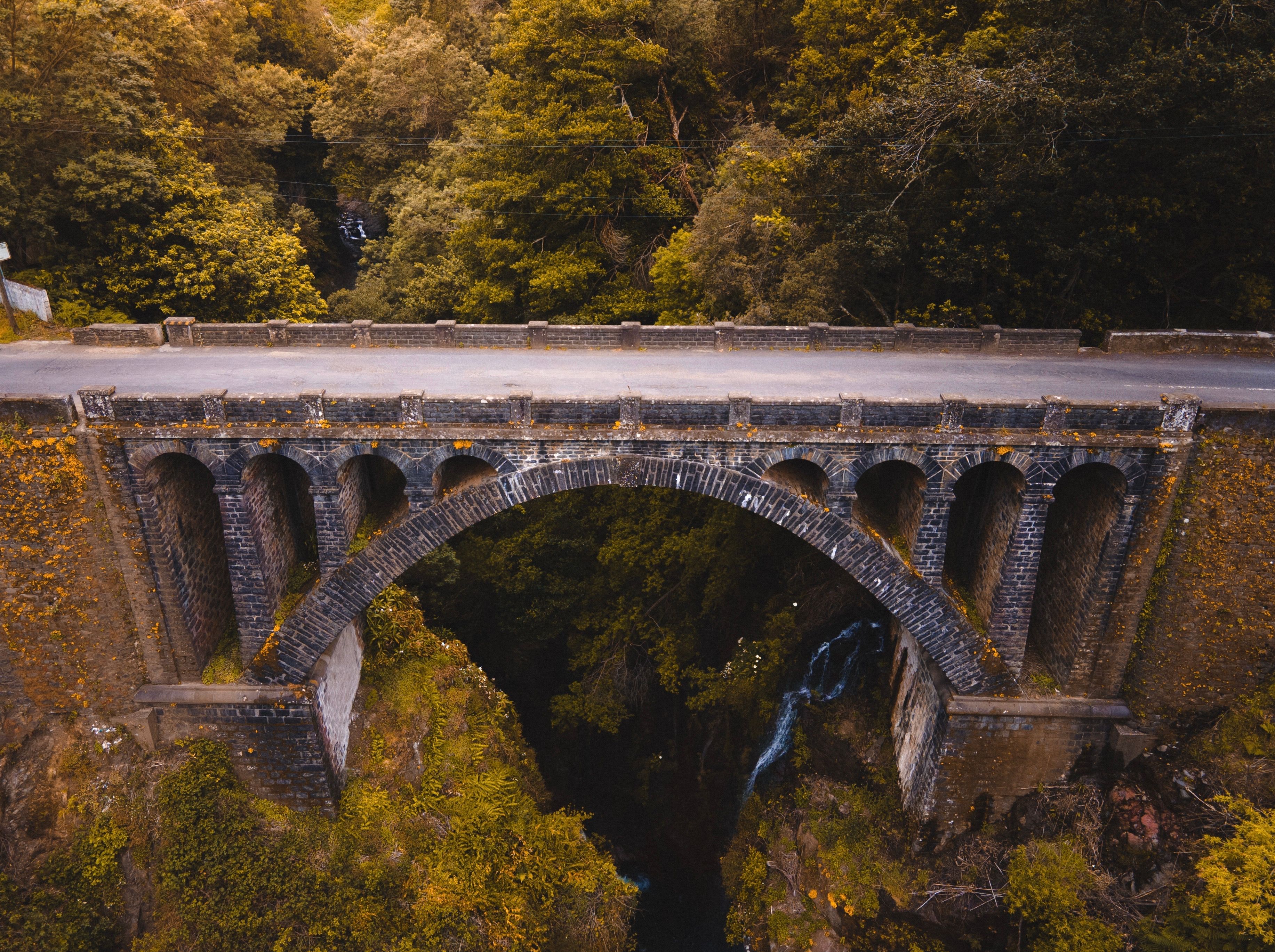 Aerial view of a historic stone bridge in Madeira, surrounded by lush greenery and dramatic landscapes.