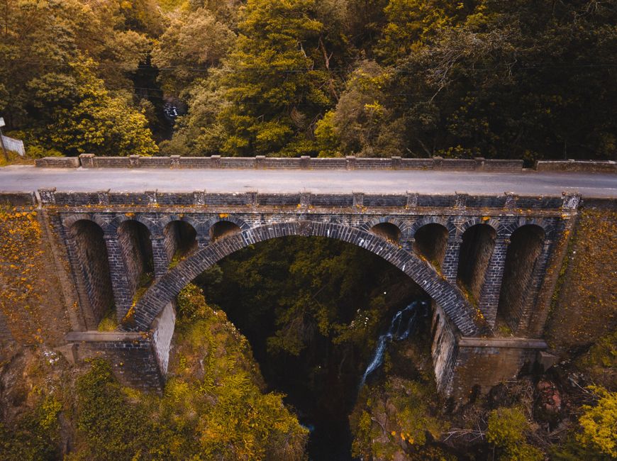 Aerial view of a historic stone bridge in Madeira, surrounded by lush greenery and dramatic landscapes.