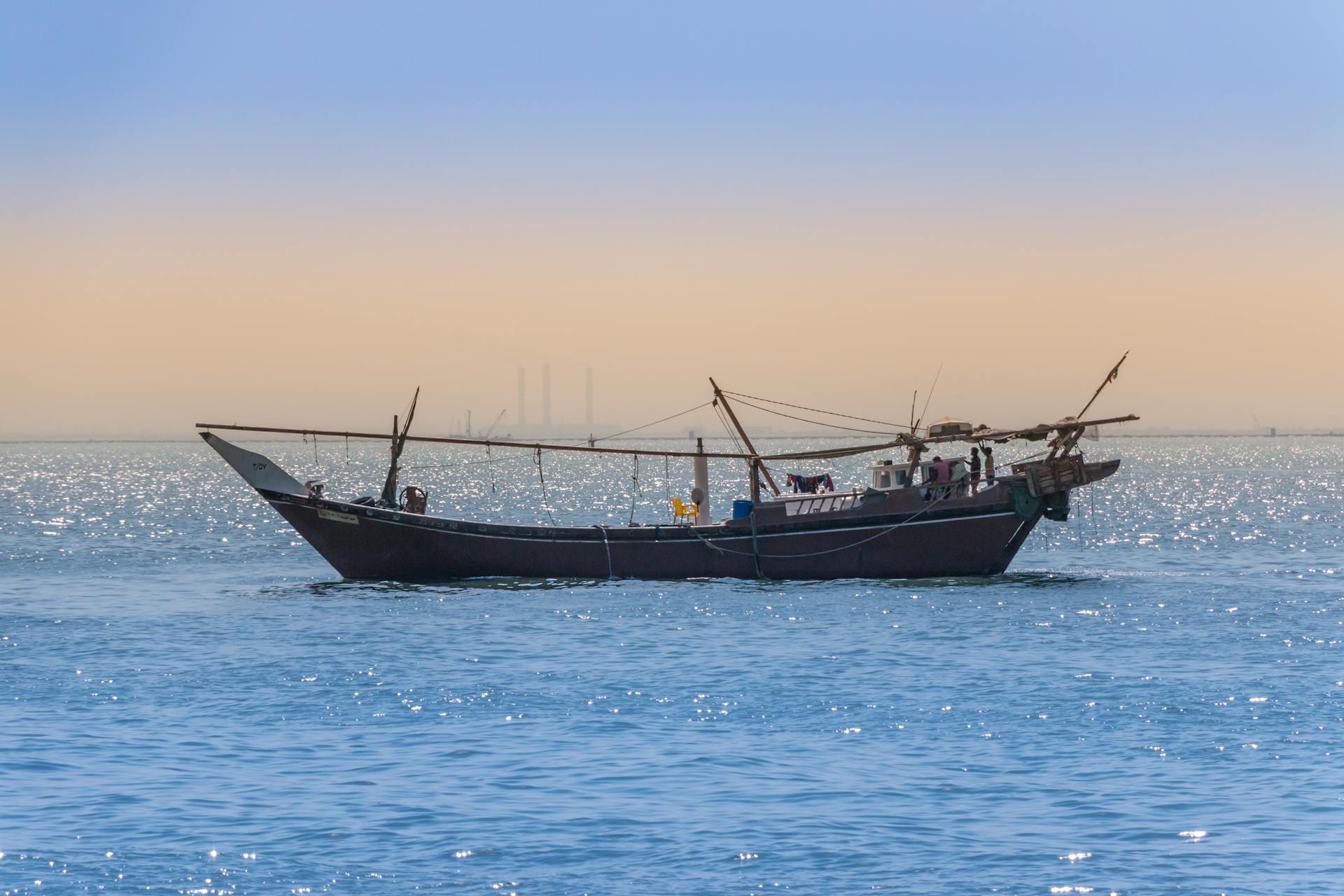 A traditional dhow boat sails peacefully on the Arabian Sea in Kuwait at dawn, with a serene backdrop.
