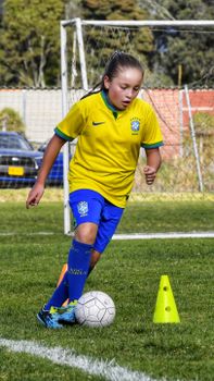 A young girl skillfully dribbles a soccer ball during practice on a sunny day outdoors.