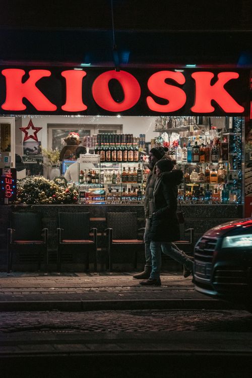 Free Neon-lit street kiosk with people walking by at night in an urban setting. Stock Photo
