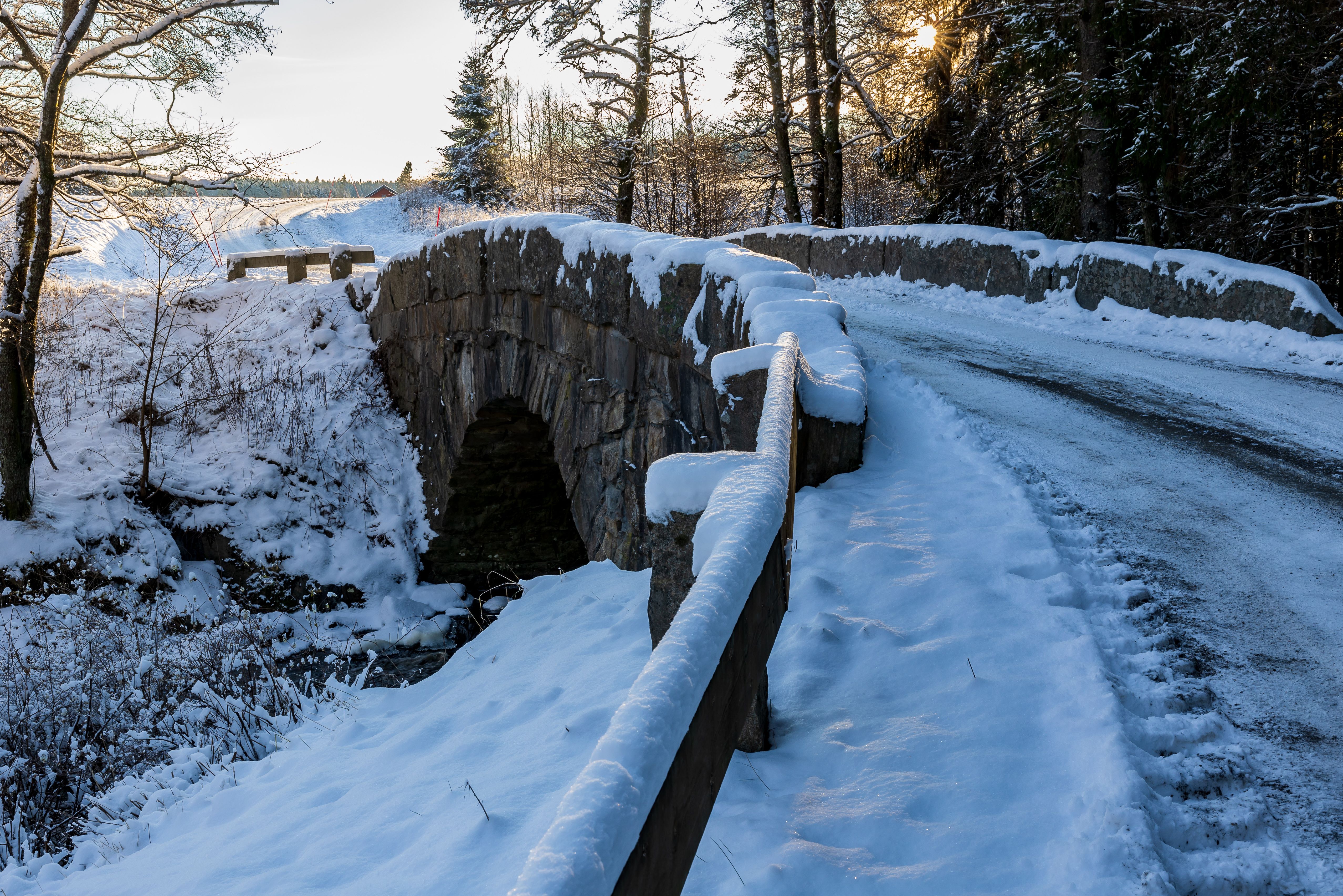A snow-covered stone bridge on a single-track road through winter forest
