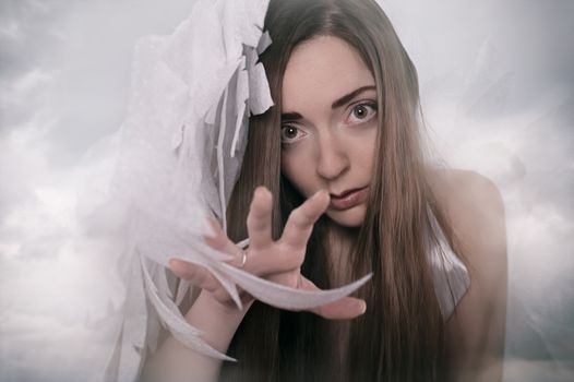 Mystical image of a woman with angel wings reaching out through clouds, evoking a celestial atmosphere.
