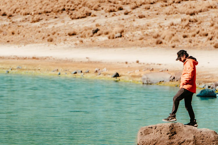 Man In Jacket Standing On Rock Over Lake