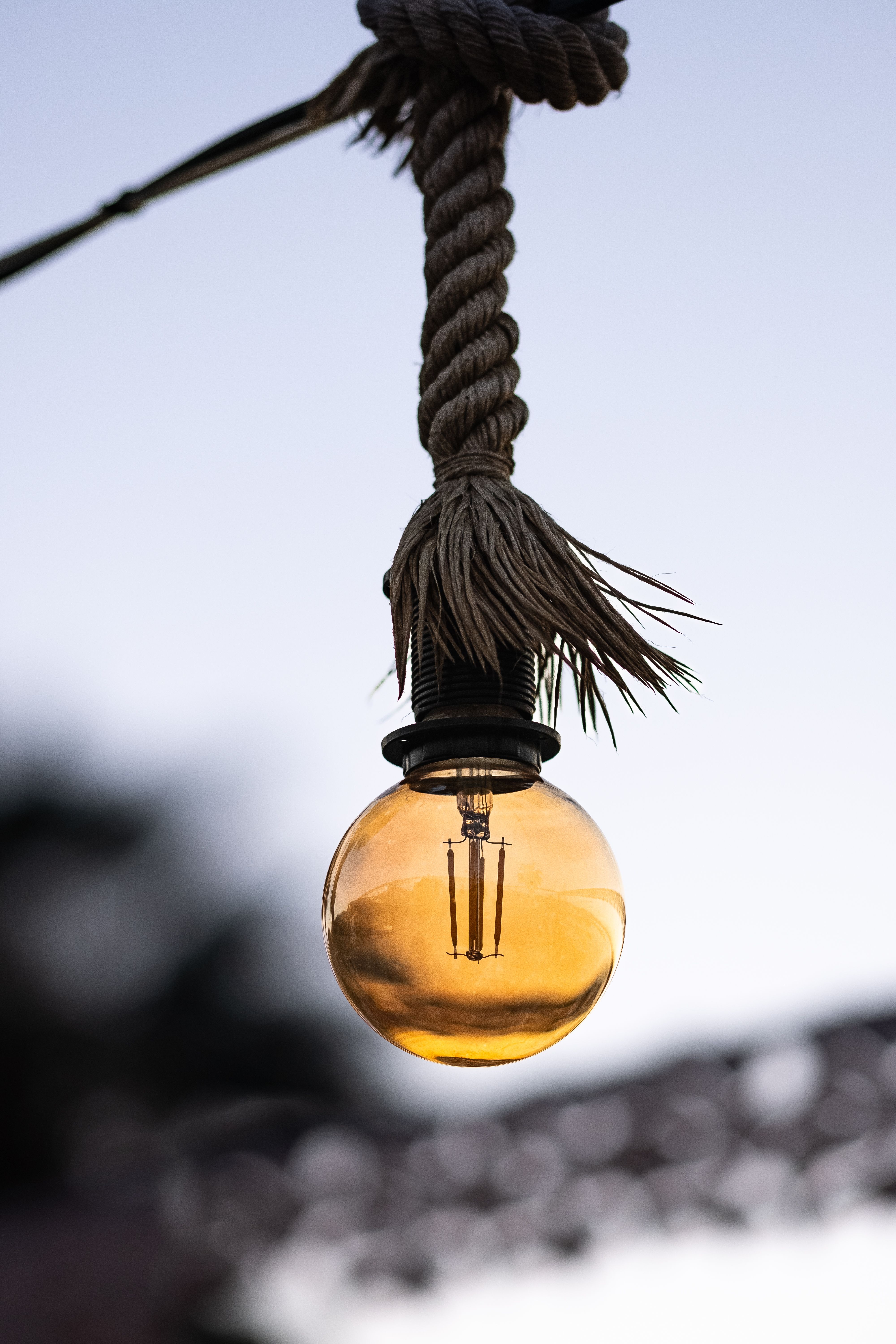 A vintage-style bulb with a warm glow hanging from a rope against a twilight sky.