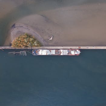 Drone capture of a cargo ship docked at the shoreline with visible greenery and sandy beach.