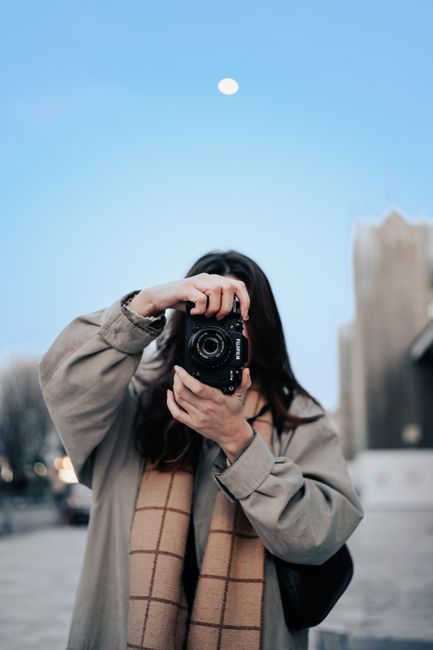 Stylish woman taking a photo with professional camera in a city environment during the day.