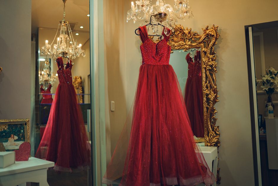 A luxurious red evening gown is reflected in a decorative mirror under a chandelier.