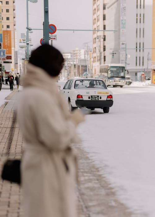 Cars on a Street in City in Winter and Woman Standing on the Sidewalk 