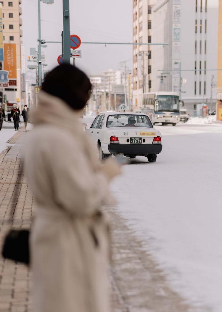 Cars On A Street In City In Winter And Woman Standing On The Sidewalk 