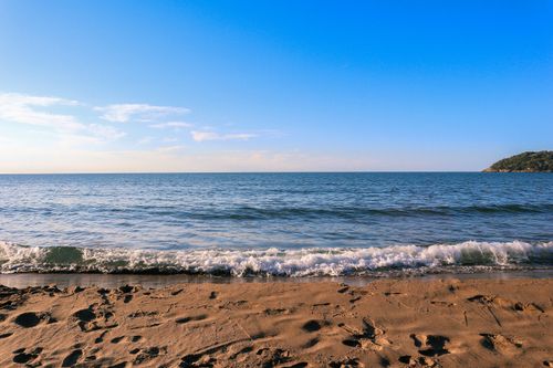 Free Relaxing beach scene with clear blue sky, gentle waves, and sandy shore, perfect for a peaceful getaway. Stock Photo