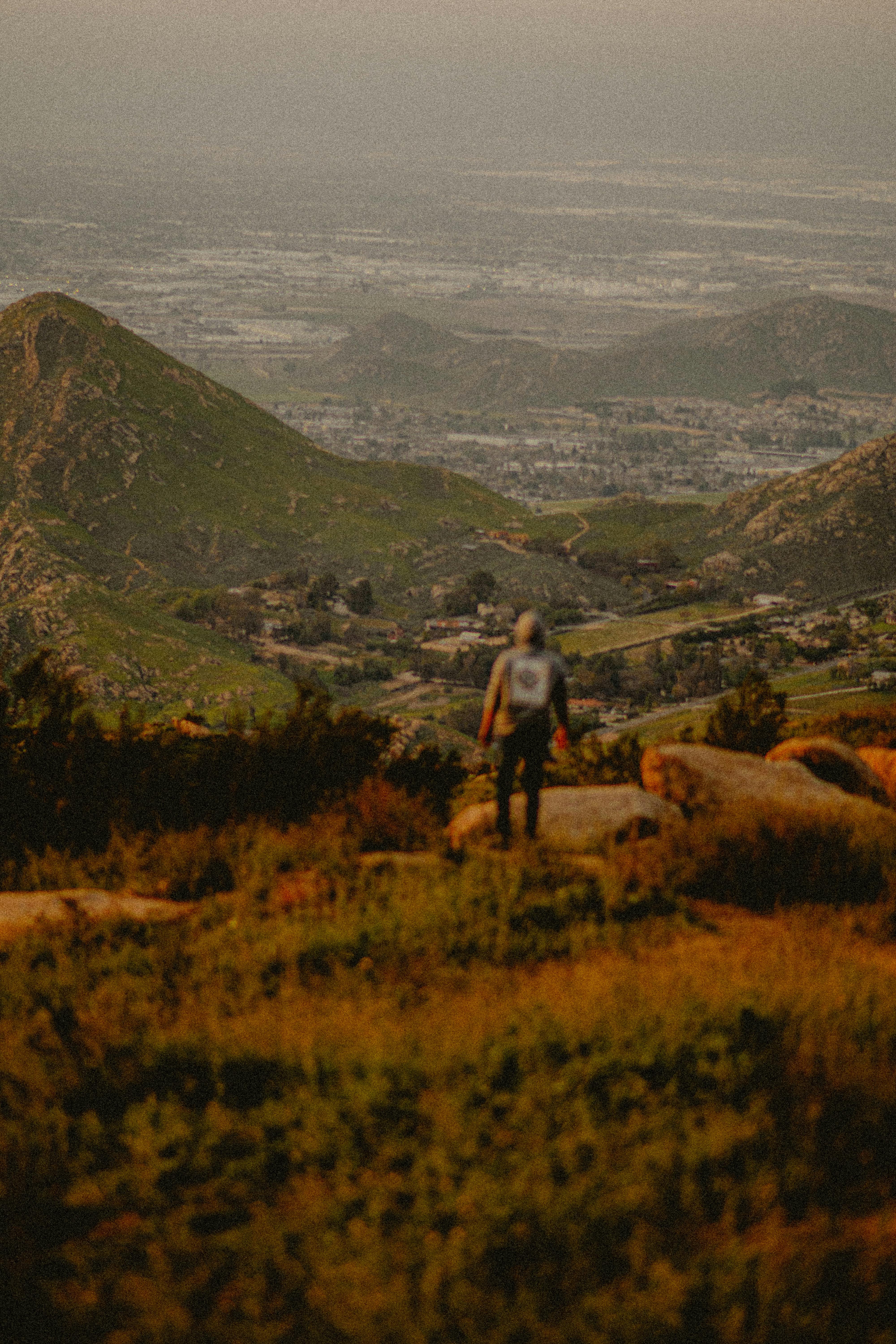 A lone hiker enjoys a tranquil view of a lush mountain valley at sunset.