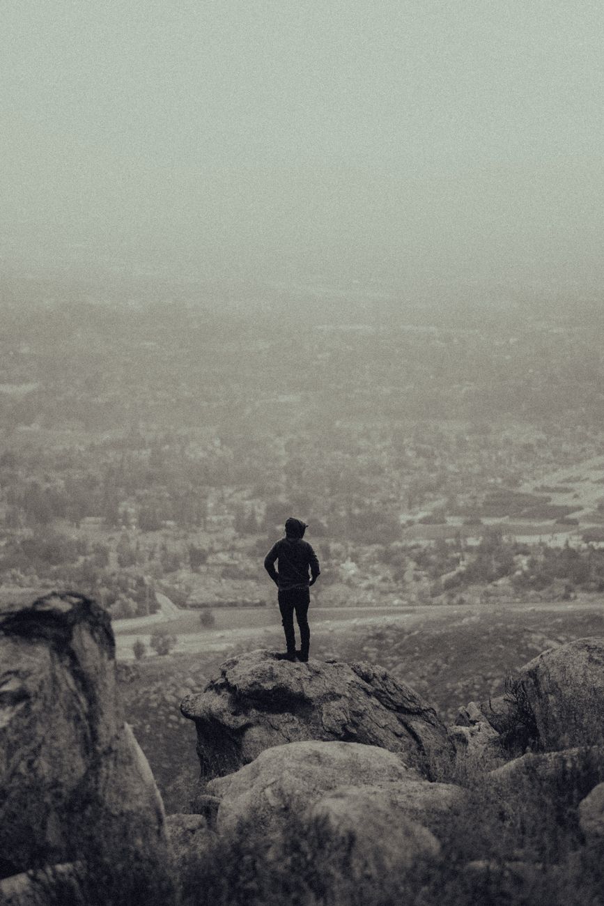 Silhouette of a person on a mountain peak, gazing across a misty, expansive valley.