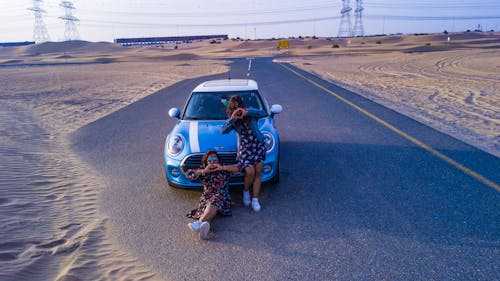 Two Women In Front Of Mini Cooper Parked In The Middle Of The Road