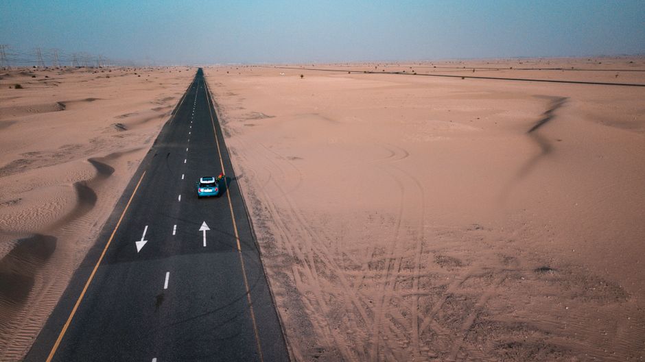 Compact rental car driving on a desert road in Jordan with mountains in the background