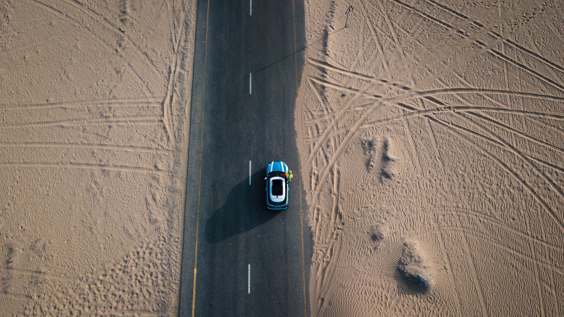 Aerial shot of a car driving on a road through the Dubai desert, showcasing travel and adventure.