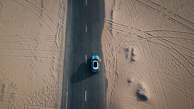 一张航拍照片中，一辆汽车正行驶在穿越迪拜沙漠的道路上，展现了旅行与冒险的主题