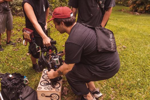 Film crew setting up a camera stabilizer outdoors, showcasing teamwork in a vibrant garden setting.