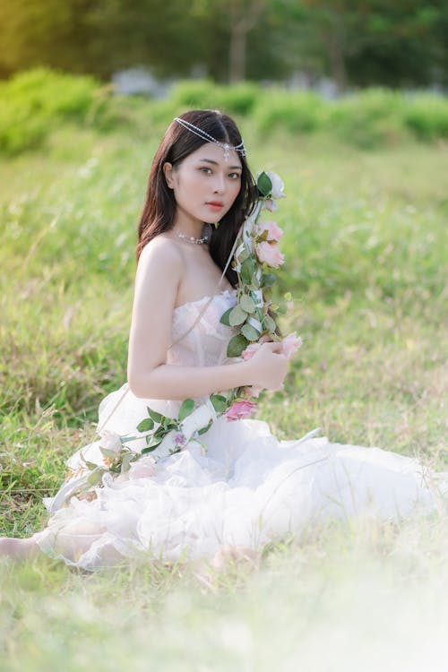 Young Brunette in a White Dress Sitting on a Field 