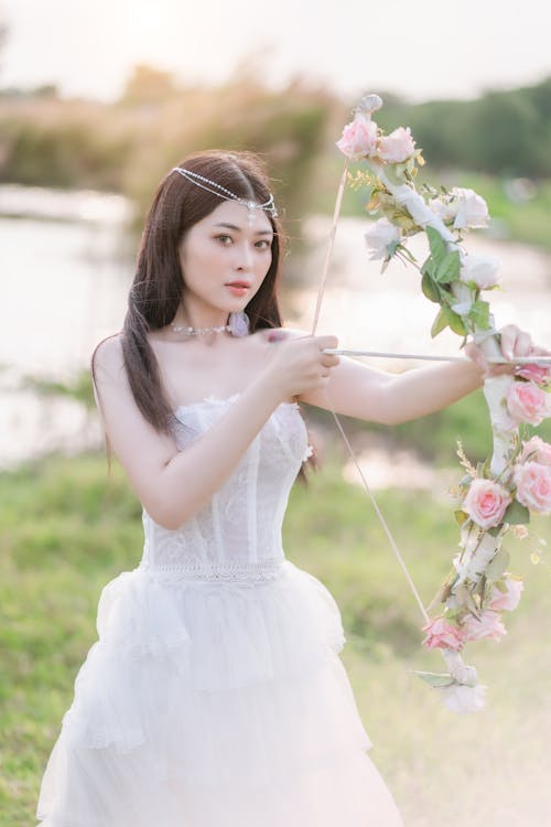 Young Woman in a White Dress Holding a Bow with Flowers 