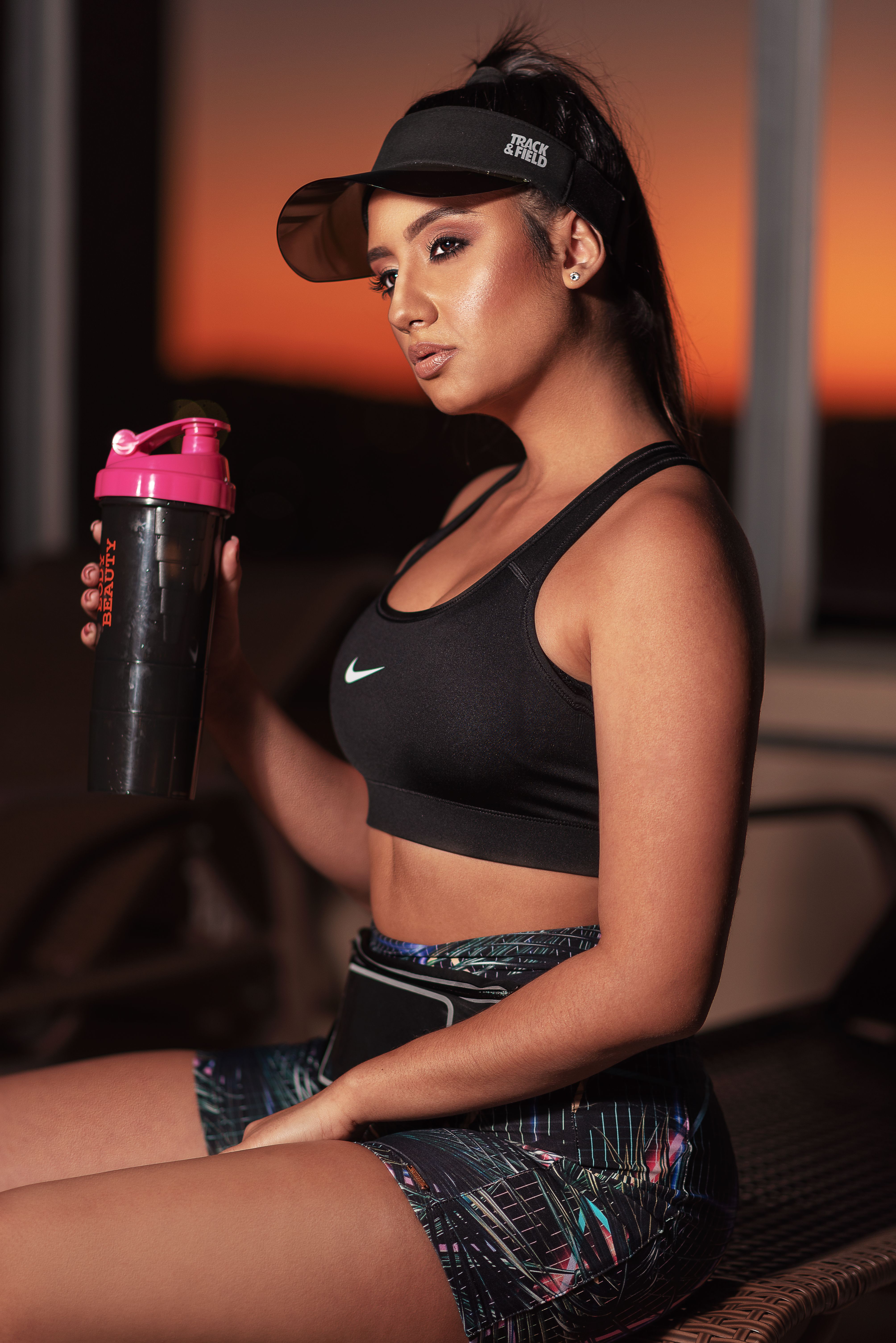 A fashionable woman in sportswear holds a shaker bottle at sunset.