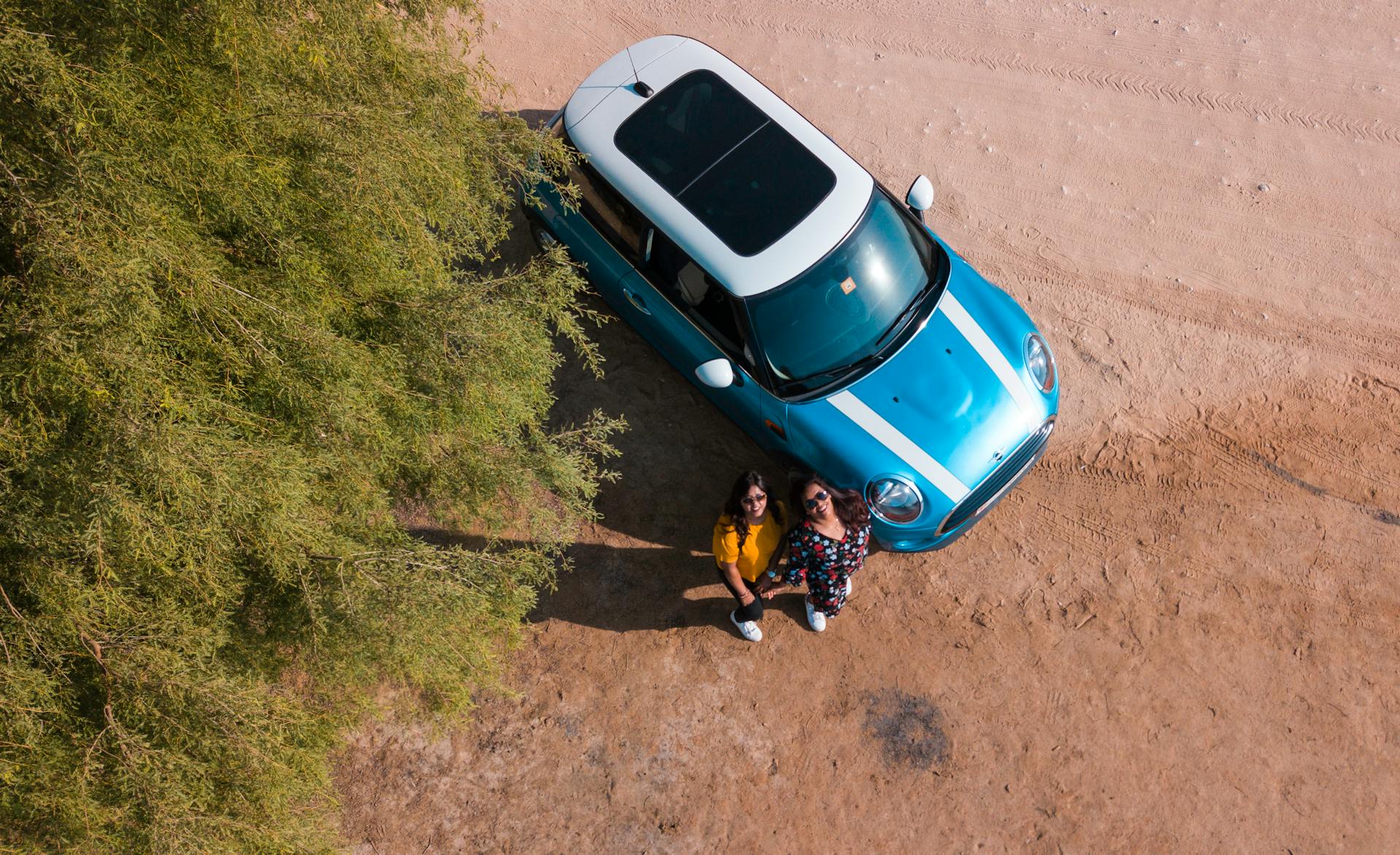 Two Woman Standing Beside Blue Mini Cooper