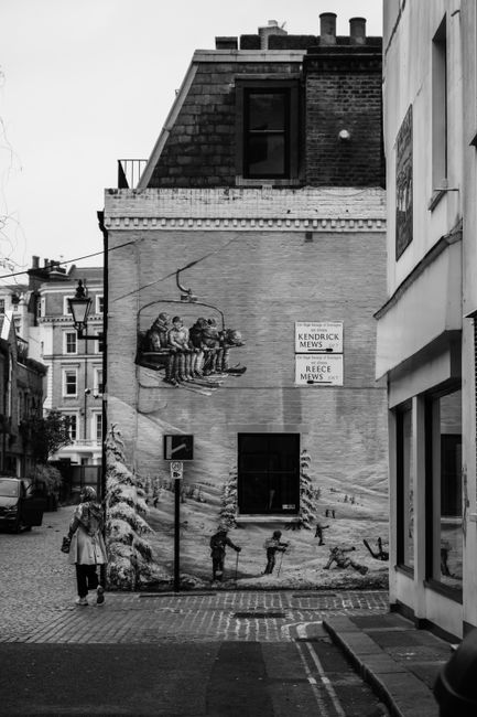 Black and white urban street scene featuring a mural on a building façade with a woman walking by.