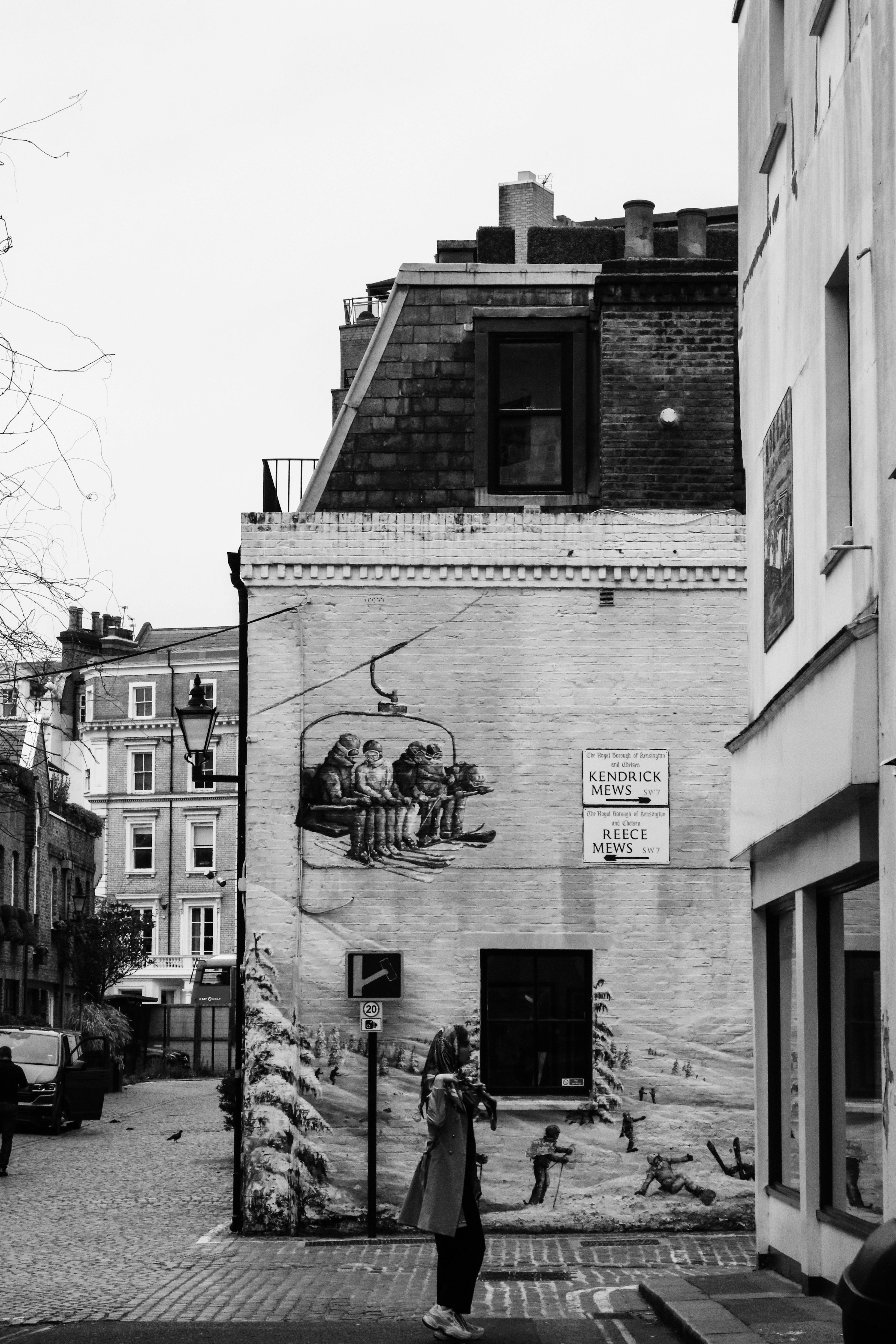 A person walks by a mural on a building in an urban setting, captured in black and white.
