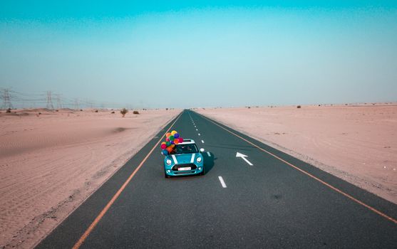 A Mini Cooper drives through the desert adorned with vibrant balloons captured from a drone view.