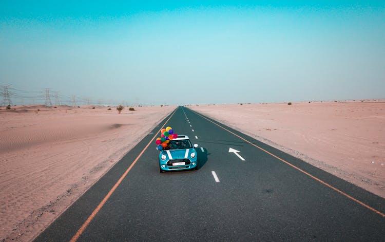 Blue And White Mini Cooper With Balloons Running On Road