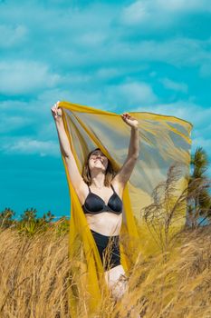 Woman in black and yellow enjoying a sunny day in a grassy field, arms raised with a smile.