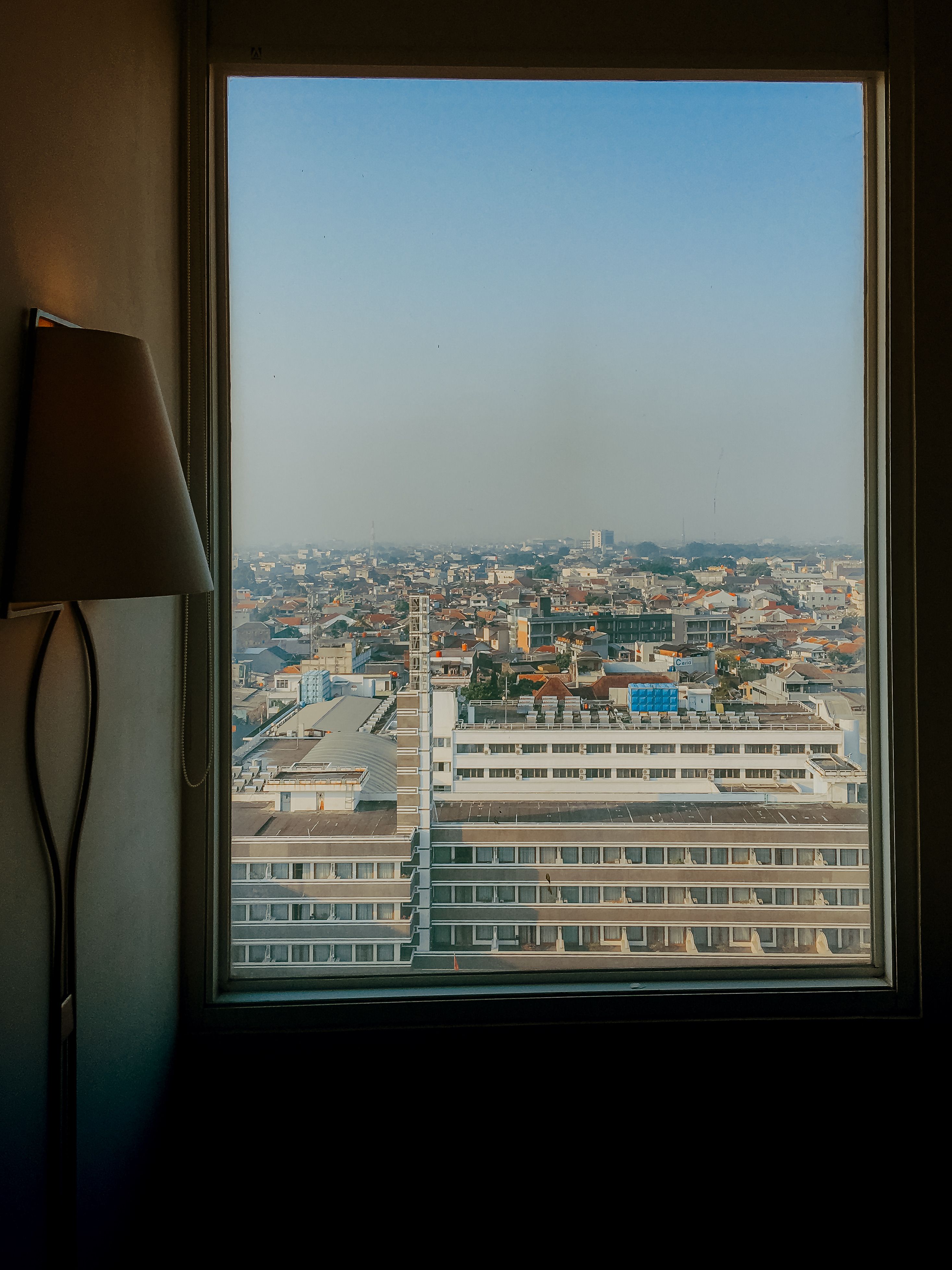 Urban cityscape of Bandung, West Java, seen through a window with a lamp in frame.