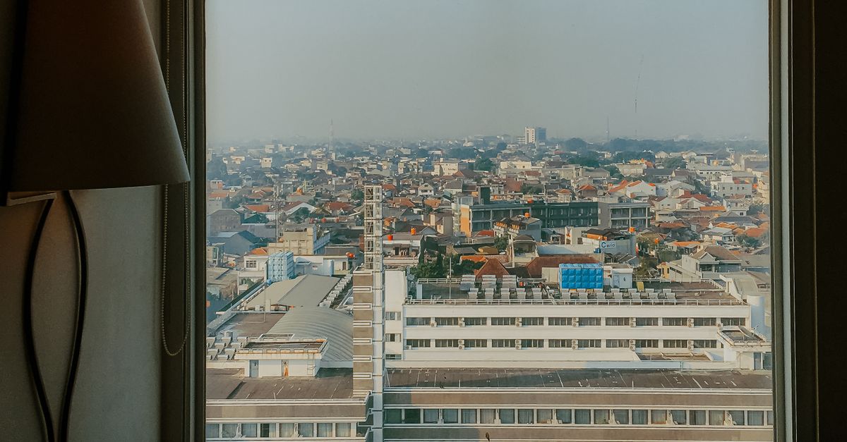 Urban cityscape of Bandung, West Java, seen through a window with a lamp in frame.