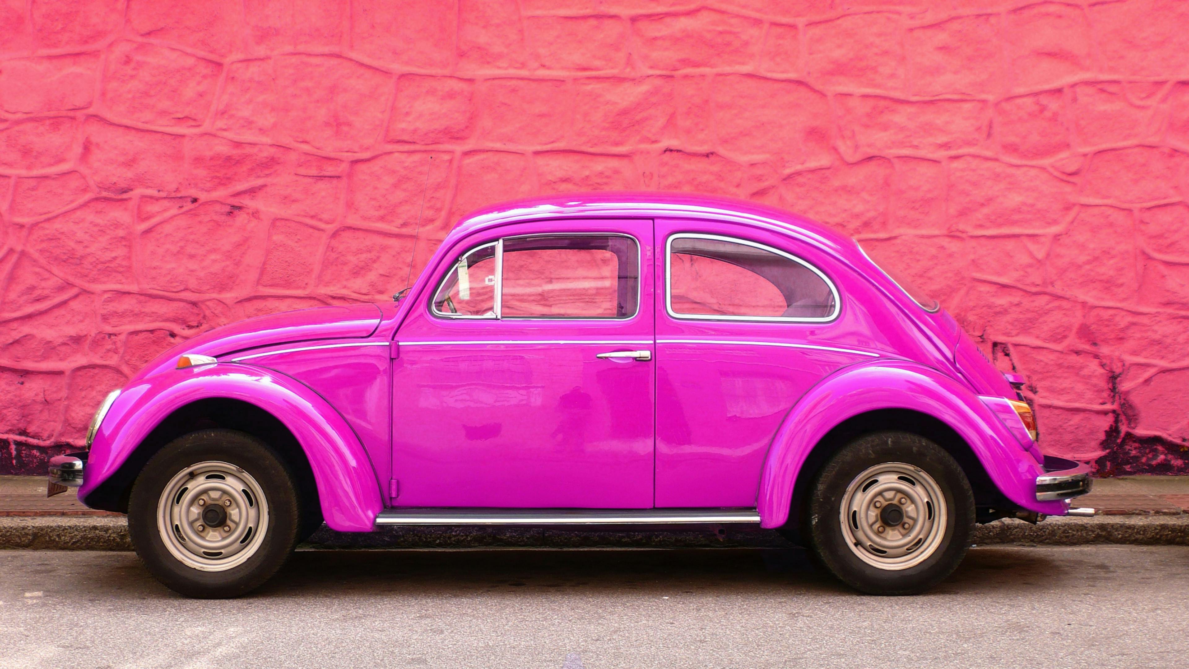 classic volkswagen beetle in hot pink parked by a pink wall