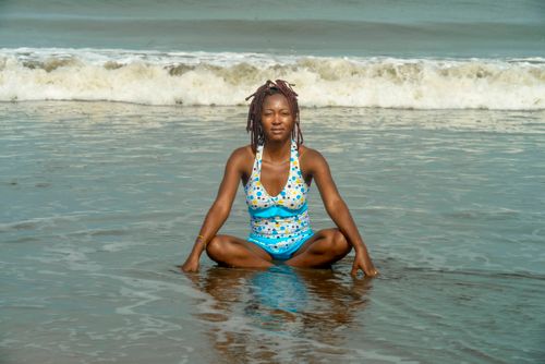 Free A black woman enjoying a relaxing moment on the beach, sitting by the sea's edge with waves in the background. Stock Photo