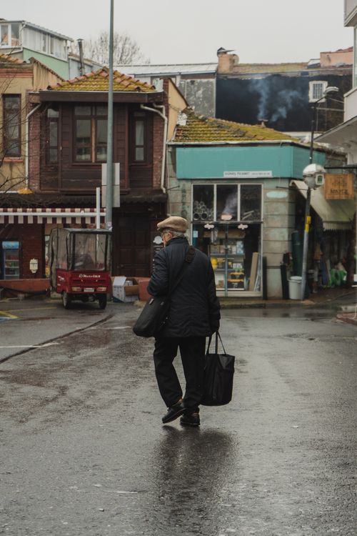Free An elderly man with shopping bags walks through a damp street in Büyükçekmece, İstanbul. Stock Photo