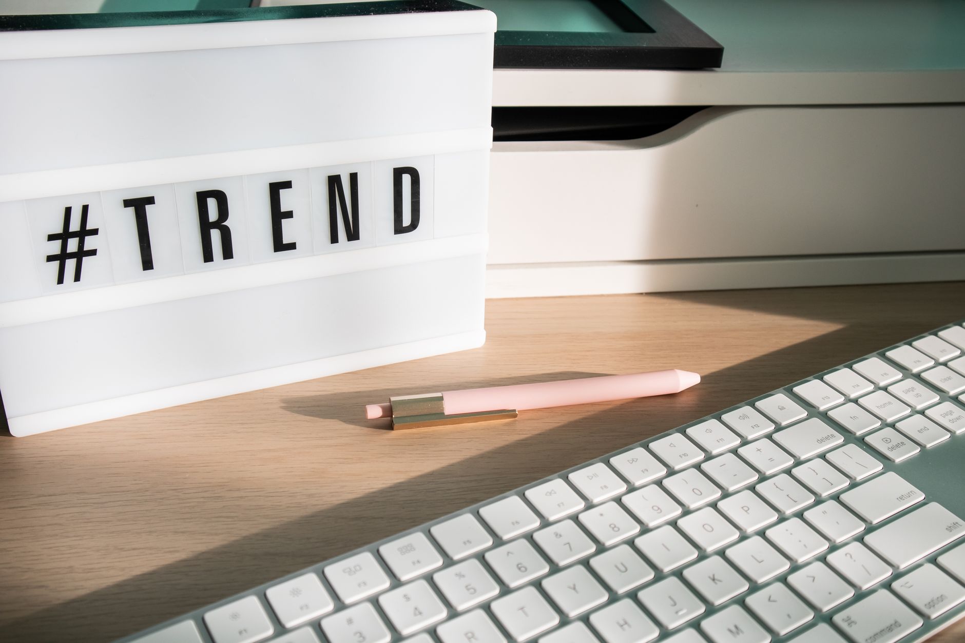 Contemporary workspace featuring a light box showing '#trend,' a pink pen, and a keyboard.