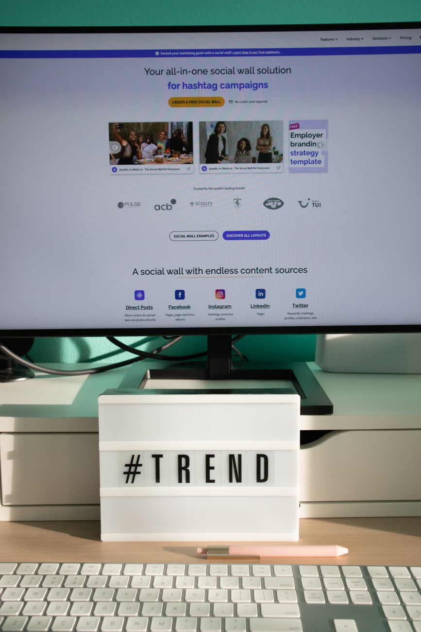 A clean and modern desk setup with a lightbox displaying '#TREND' and a computer monitor showing a social wall solution.