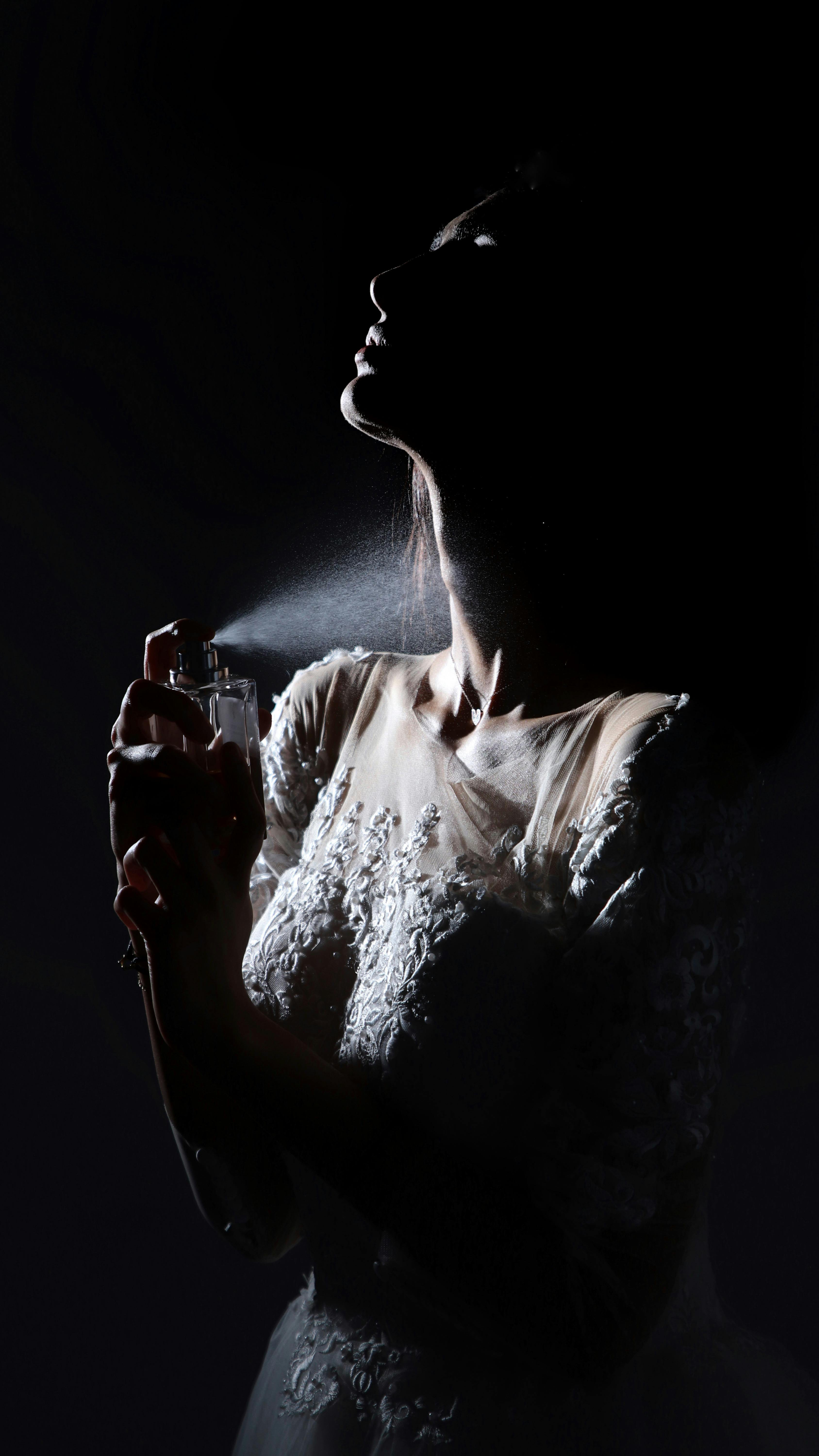 Artistic black and white portrait of a bride in a shadowy ambiance applying perfume before her wedding.