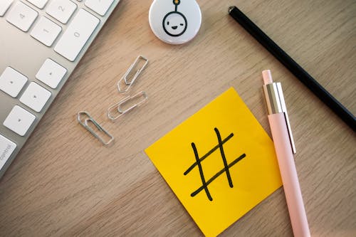 Free Top View of a Keyboard, Paper Clips, Pencil and a Sticky Note with a Hashtag on It Lying on a Desk Stock Photo