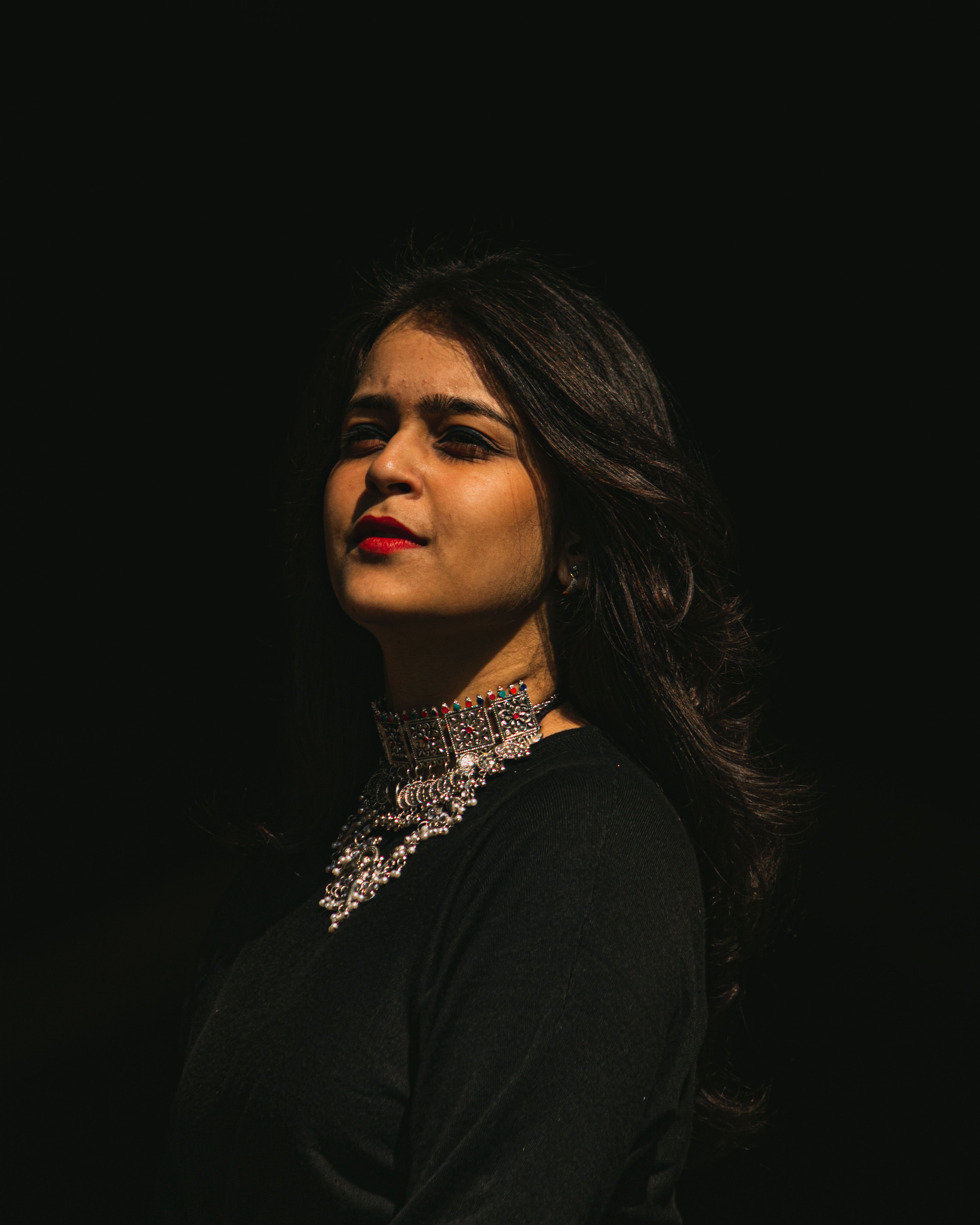Portrait of a woman with striking red lips and intricate necklace against a black background.