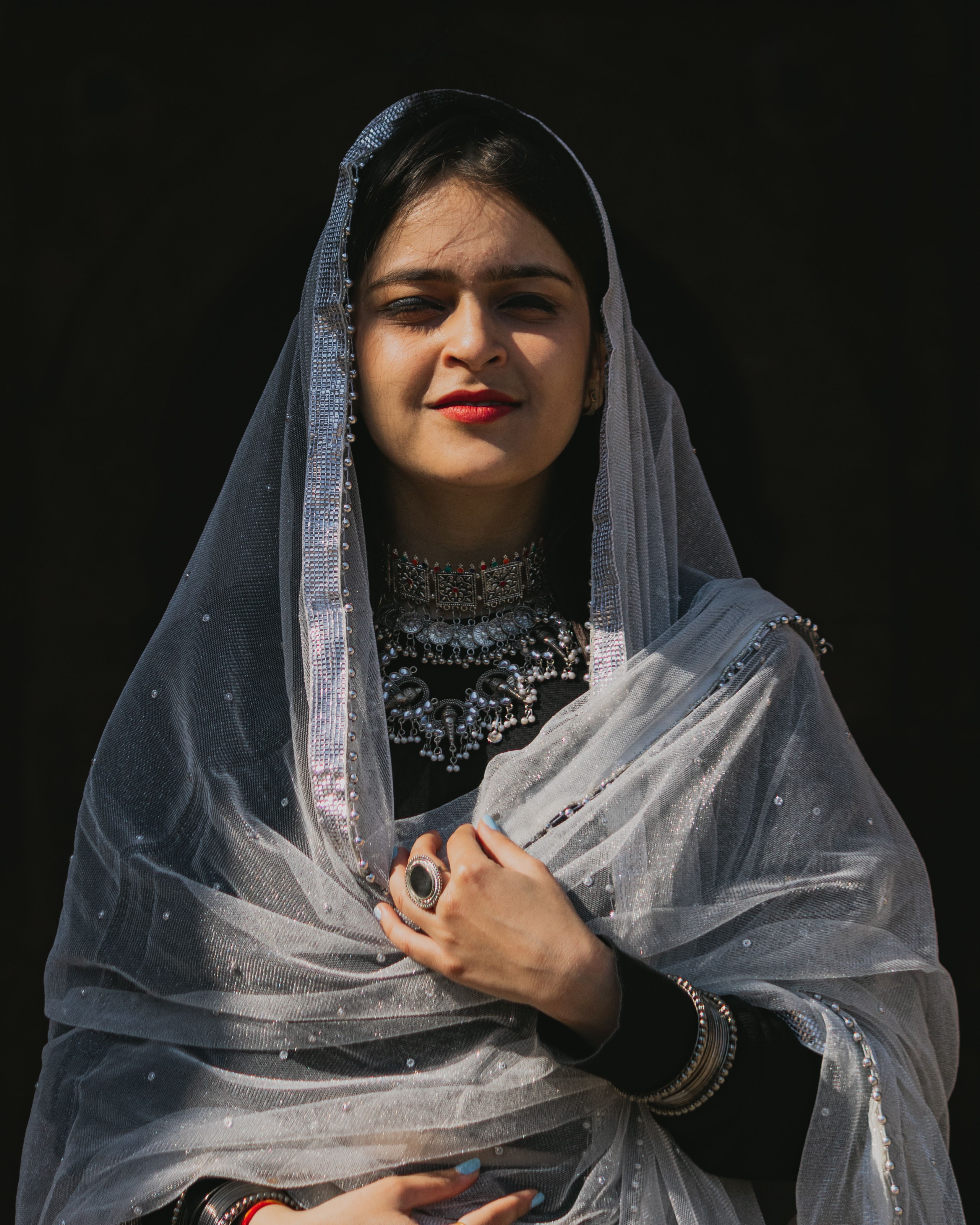 Woman in traditional silver veil and jewelry against black background. Elegant and serene.
