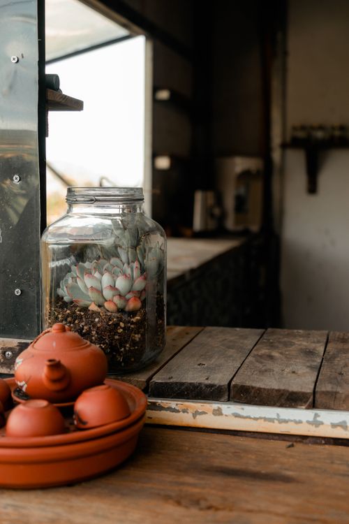 Free A cozy indoor setting featuring a succulent terrarium in a glass jar and traditional teapot on a wooden surface. Stock Photo
